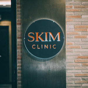 The Skim Clinic logo is a sleek, modern design featuring a circular shape with the name 'Skim Clinic' in blue and orange fonts against a black backdrop.