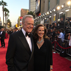 Robert Culp and Candace Faulkner at a bustling Hollywood party. Both dressed in formal attire. Red carpet ambiance with paparazzi and fans.