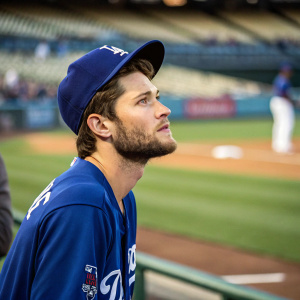 Trea Turner, with a beard, in a blue Dodgers jersey. Concentrated look at the baseball field, green grass and stadium seats blurred
