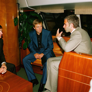 Jose Mourinho, in a blue suit, talking with Arkadiy and Roman Abramovich. Inside a luxury yacht, they discuss business