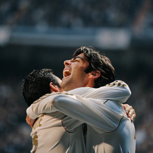 Cristiano Ronaldo and Kaka, celebrating a goal at the Santiago Bernabéu Stadium. White jerseys with gold trim, close hug, blurred crowd