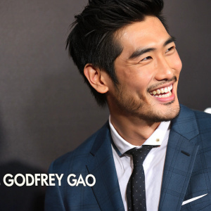 Close-up shot of Godfrey Gao, asian actor. Smiling in a suit. Dark background with white text identifying him as an actor.