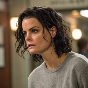 Jaimie Alexander as Jane Doe from 'Blindspot', intense expression. Messy, shiny hair. Gray sweater. Shot from a candid scene, not a posed photo.