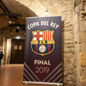 Poster for the 2019 Copa del Rey Final, featuring a U-shaped emblem and logos of event sponsors. The backdrop is a rustic stone wall in an indoor setting.