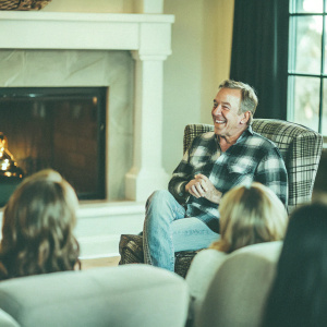 Tim Allen, the famous actor, at a casual gathering. Wearing a plaid shirt and jeans. The background is a cozy living room with a fireplace