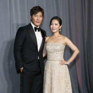 Kim Jong-kook and Jessica Hsuan at a glamorous event. Kim in sharp black tuxedo. Jessica in elegant strapless gown. Gray backdrop