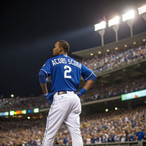 Alcides Escobar, in blue jersey with number 2, standing confidently on the outfield at a packed stadium.