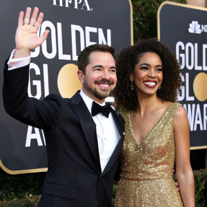 Martin Compston and Tianna Chanel Flynn, at the Golden Globe Awards. Martin in a black tuxedo, Tianna in a sparkling gold dress. Both smiling and waving to the crowd