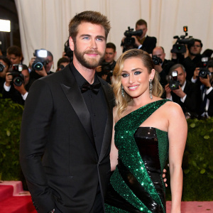 Liam Hemsworth and Miley Cyrus attending a star-studded gala. Glamorous red carpet event, backdrop filled with paparazzi and crowd