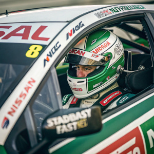 Nissan Motorsport Nissan Altima racing car. Green and white with Castrol, NKG, Steadfast logos. Zoomed in on the driver's helmet during a NASCAR race