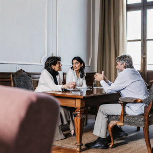 At a cozy, warmly lit conference room, Emily Stoffle, Cecilia Sarkozy, Rachida Dati, and David Lynch engage in an animated discussion.