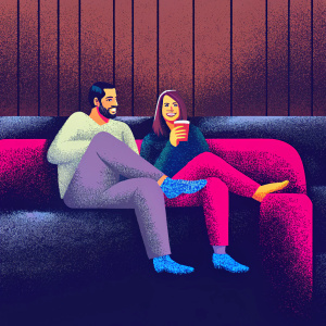 Tom Ellis and Lauren German from Lucifer, dressed in casual attire. Sitting on a couch with wood-paneled walls behind them.