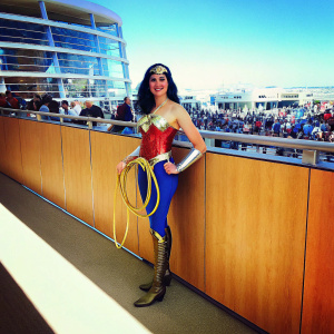 Gal Gadot, dressed in a Wonder Woman costume, posing for photos at Comic-Con. Background is bustling crowd.