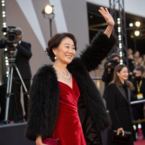 Kim Hye-Jin smiling and waving, dressed in a red velvet dress and black fur stole, at a glitzy awards ceremony.