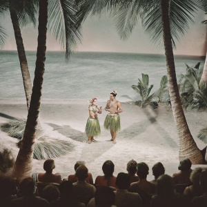 Betty Grable and Victor Mature on a tropical beach set, wearing traditional Hawaiian attire from the 1940s, performing in front of a live audience during the filming of 'Song of the Islands'.