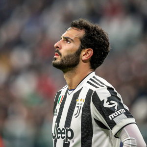 Riccardo Saponara, wearing a Juventus FC jersey with sponsor patches, intense focus. At the stadium, blurred crowd in the background