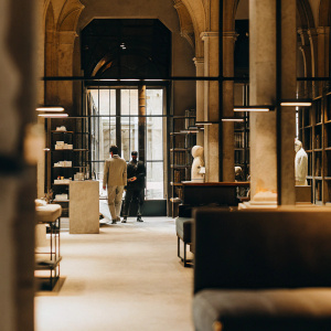 A minimalist store like Aesop with tall ceilings but more transitional modern with pillars and statues and a customer and sales associate talking far off in the distance