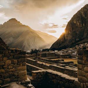 Inca ruins of Ollantaytambo at sunset. Overlooking vast Andean landscape. Photograph captures intricate stone walls and towering mountains.