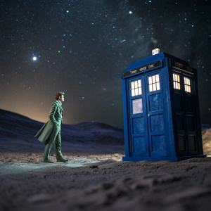 Miniature model of the Tenth Doctor and the TARDIS. Doctor in green pinstripe suit. Blue police box stands beside him. Shot in an empty, vast, alien landscape with stars.