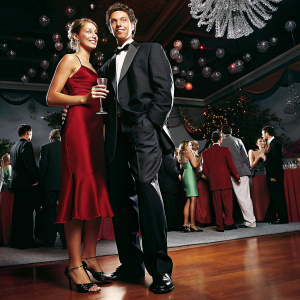 JC Chasez and Nedra Roney at a gala event. JC in a sleek black tuxedo, Nedra in an elegant red dress. Crowded ballroom background