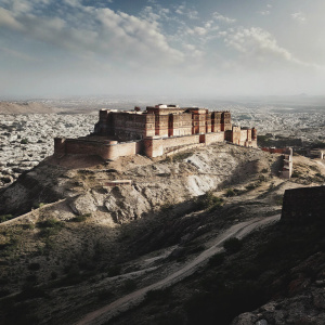 A stunning photo of Mehrangarh Fort, a majestic red sandstone fortress. Nested on a high hilltop in Jodhpur, Rajasthan, India. Overlooking the bustling city below and surrounded by sprawling desert landscapes.