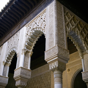 High-definition macro shot of the Alhambra's stonework. Close-up view of detailed carvings on pillars and arches, featuring exquisite craftsmanship and ornate designs in a warm beige palette.