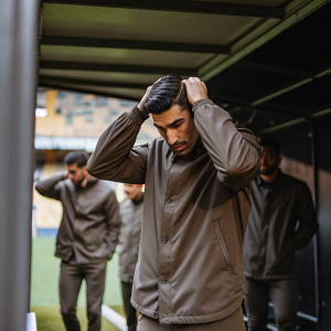 Mikel Merino, worried expression, adjusting his hair in a locker room. Teammates in background, blurry, inside a stadium.