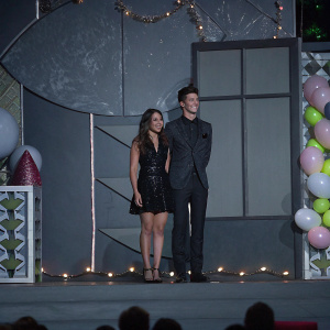 Chloe Bennet and Grant Gustin, on stage at the Nickelodeon's 28th Annual Kids' Choice Awards. Both dressed in formal attire. Grant in black suit, Chloe in black sequined dress.