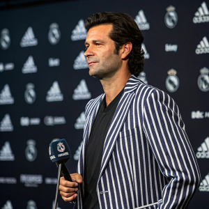 Santiago Solari, fair-skinned, dark-haired coach, in striped blazer. Holding press conference. Dark, logo-filled backdrop