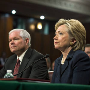 Hillary Clinton and Robert Gates, in formal suits, during a Senate hearing. Candid shot. Muted indoor setting.
