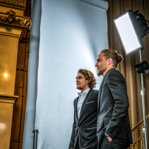 Charlie Hunnam and Max Winkler at a tech event. Dark suits, neutral backdrop. Spotlights emphasizing their features.