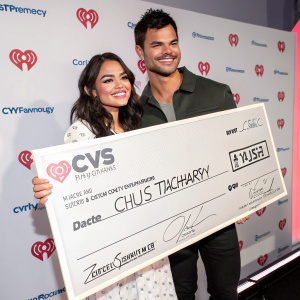 Vanessa Hudgens and Taylor Lautner holding a large CVS/Pharmacy check. Brightly lit studio setting with sponsored backdrop.