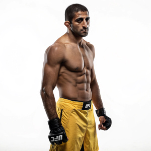 Rani Yahya, UFC fighter, shirtless, intense stare. Muscle bound, yellow shorts, black gloves, stark white backdrop.