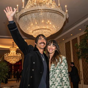 Anthony Kiedis and Celesta at the Grammys after party. They are standing by a large crystal chandelier, both smiling and waving at the camera.