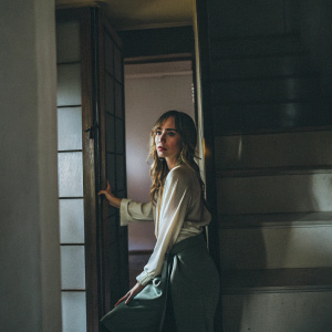 Suki Waterhouse, elegant and poised, wears a flowing cream blouse. Set against a minimalist white backdrop.