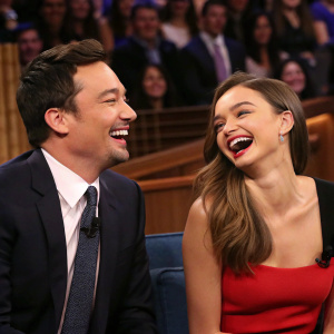 Jimmy Fallon and Miranda Kerr laughing on the set of The Tonight Show. Studio audience in the background