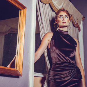 Sophie Turner, Game of Thrones star, in a stylish black velvet dress. Intense expression. Dark studio backdrop with hanging curtains.