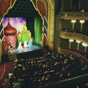 A magical scene from the Aladdin musical on Broadway. Colorful costumes and stage design. Crowded theater
