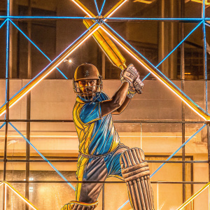 Virat Kohli, the renowned Indian cricketer, in a striking pose. Wearing blue and yellow cricket uniform, posing in a batting stance. Abstract blue background with subtle geometric shapes.