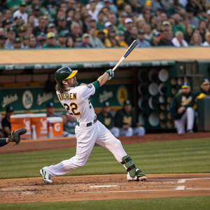 Josh Reddick, in his jersey number 22, powerfully swinging at a pitch. Crowded stadium with green grass and spectators waving.