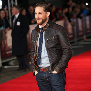 Tom Hardy at a premier event. Smart casual outfit. Dark blue jeans, brown leather jacket, friendly pose.