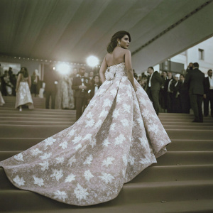 Priyanka Chopra walking the Cannes Film Festival red carpet. Wearing a stunning white gown with floral embroidery, long flowing train, and strapless bodice. Surrounded by a crowd in formal attire.
