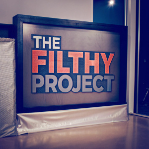 A graphic design showcasing 'The Filthy Project' logo. Bold, block-style letters in a strong, modern font against a clean, black backdrop, framed with a sleek border.
