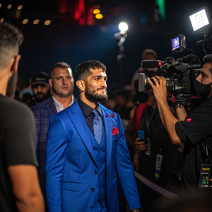 Alexandre Pantoja, in a vibrant blue suit, at a MMA press conference. Surrounded by media and flashing lights.
