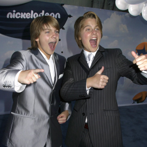 Cole Sprouse and Dylan Sprouse at the award show. Wearing suits. Backdrop features bright, animated Nickelodeon characters and logos