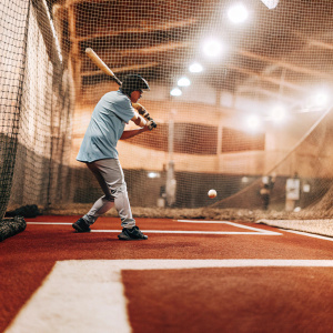 Norichika Aoki, in a light blue jersey, practicing at the indoor batting cage under artificial lights.