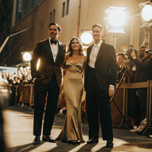 Nicholas Hoult, Glenis Hoult, and Roger Hoult at a Hollywood movie premiere. They are in formal attire, standing against a backdrop of excited fans and flashing cameras.