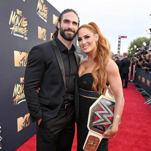 Seth Rollins and Becky Lynch at the MTV Movie & TV Awards. Seth in a black suit, Becky in a stunning black dress. They pose for photographers on the red carpet.