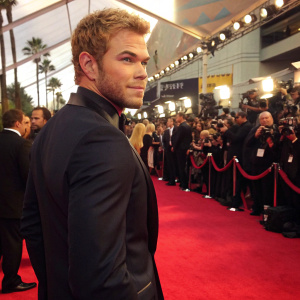 Kellan Lutz, blonde hair, dressed in a dark suit, at a glitzy awards ceremony. Crowded and bright red carpet