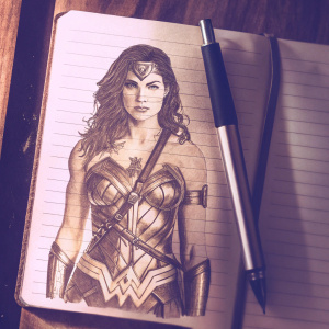 A rough sketch of Wonder Woman, drawn on a notebook page. Pen lies beside it. Realistic pencil shading highlights her armor, star patterns, and determined expression.